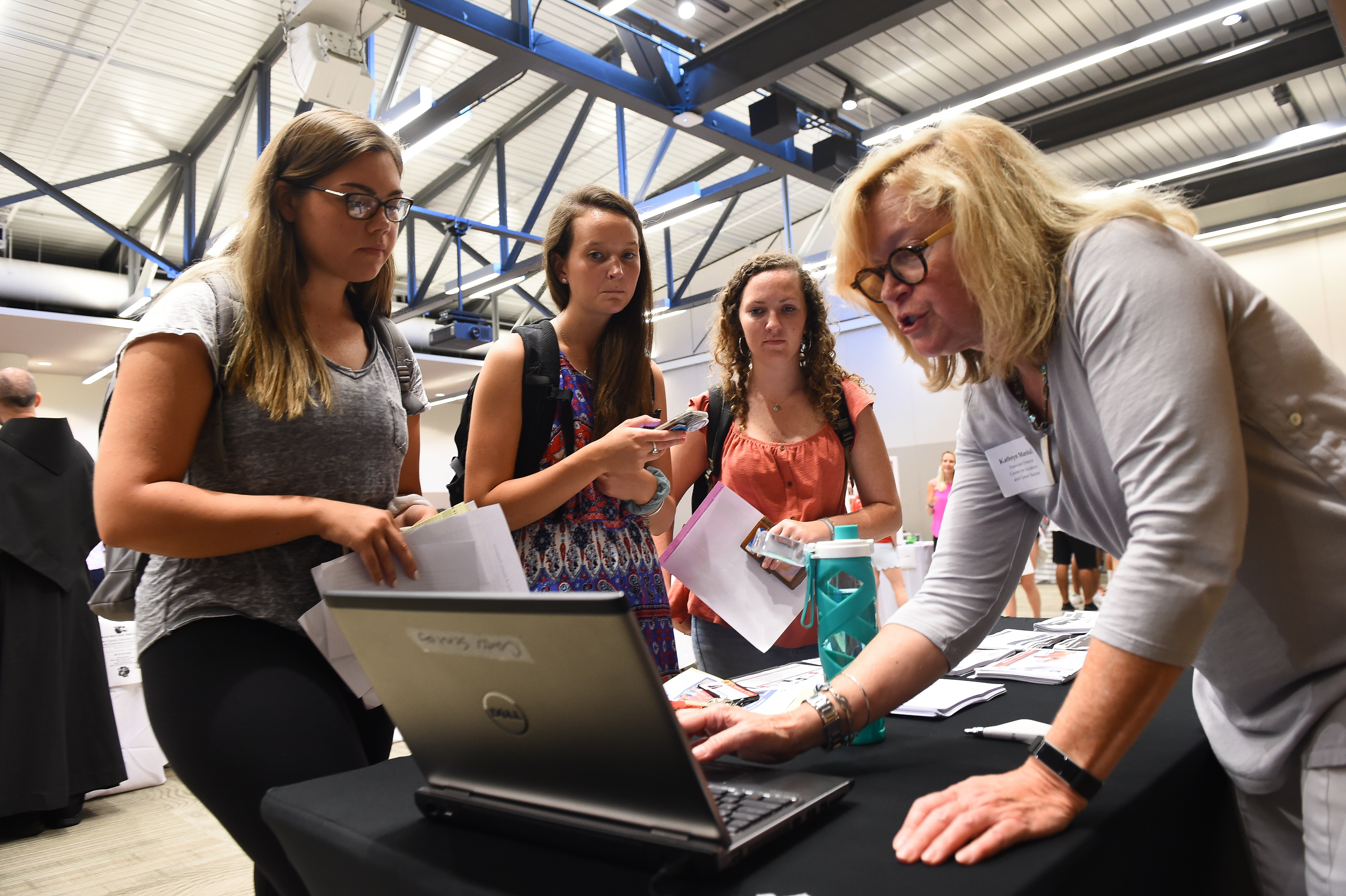 Three Catholic University students stand around a table at the Campus Employment Fair, looking as an older woman displays something on a laptop.