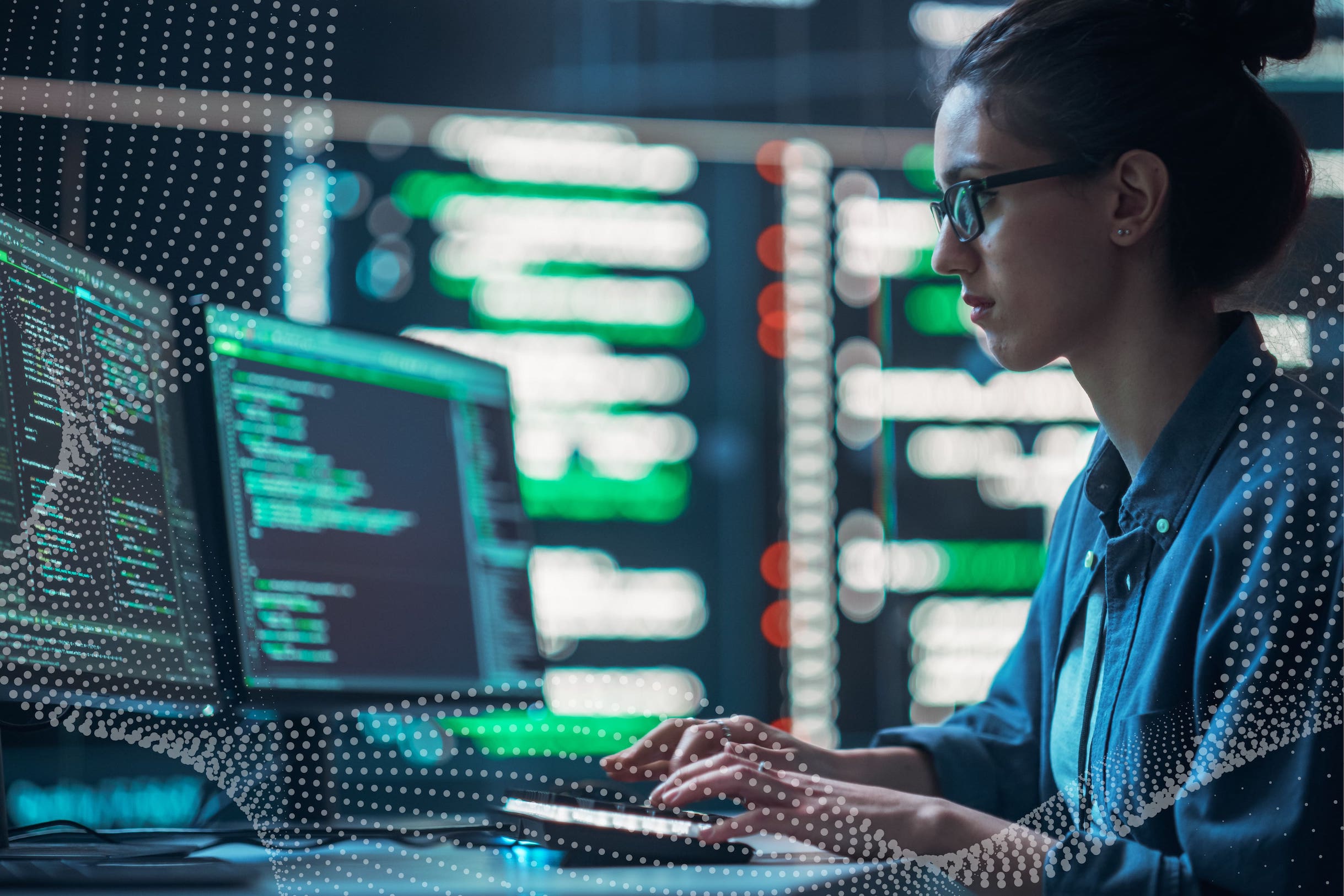 Woman in glasses staring at dual monitors, with data, typing