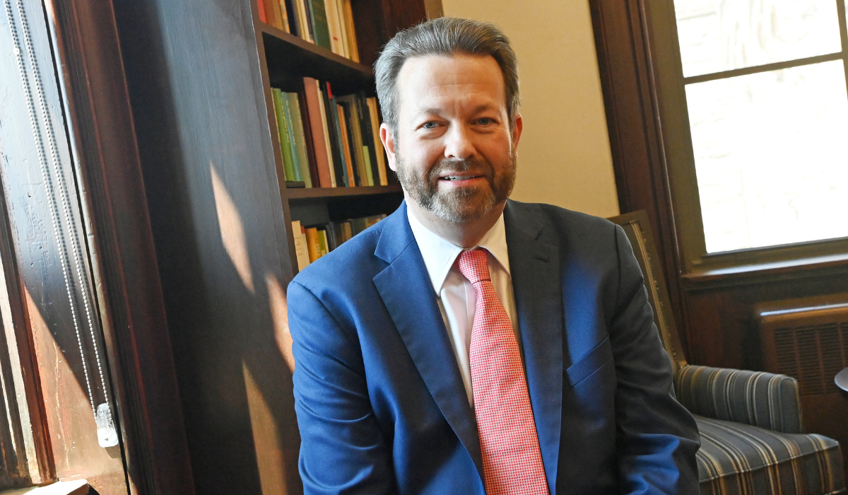 Dr. Kurt Martens is sitting in a library, in front of a shelf of books.