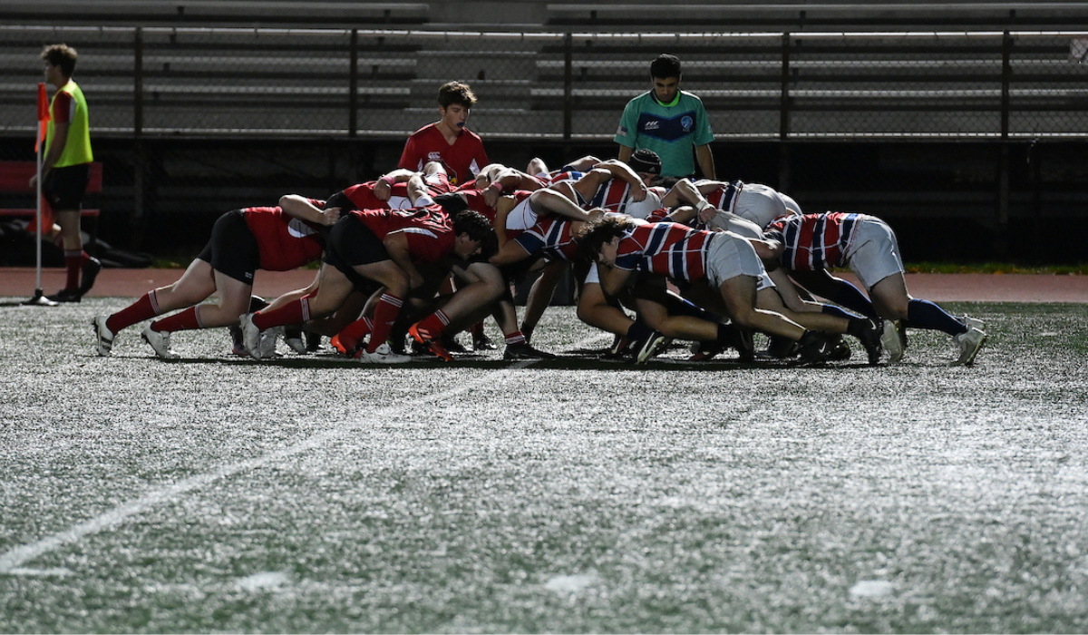 The rugby team is huddled on the field, which is sprinkled with snow.