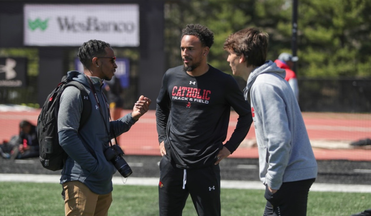 Malachi is speaking with two fellow Cardinals on the football field.
