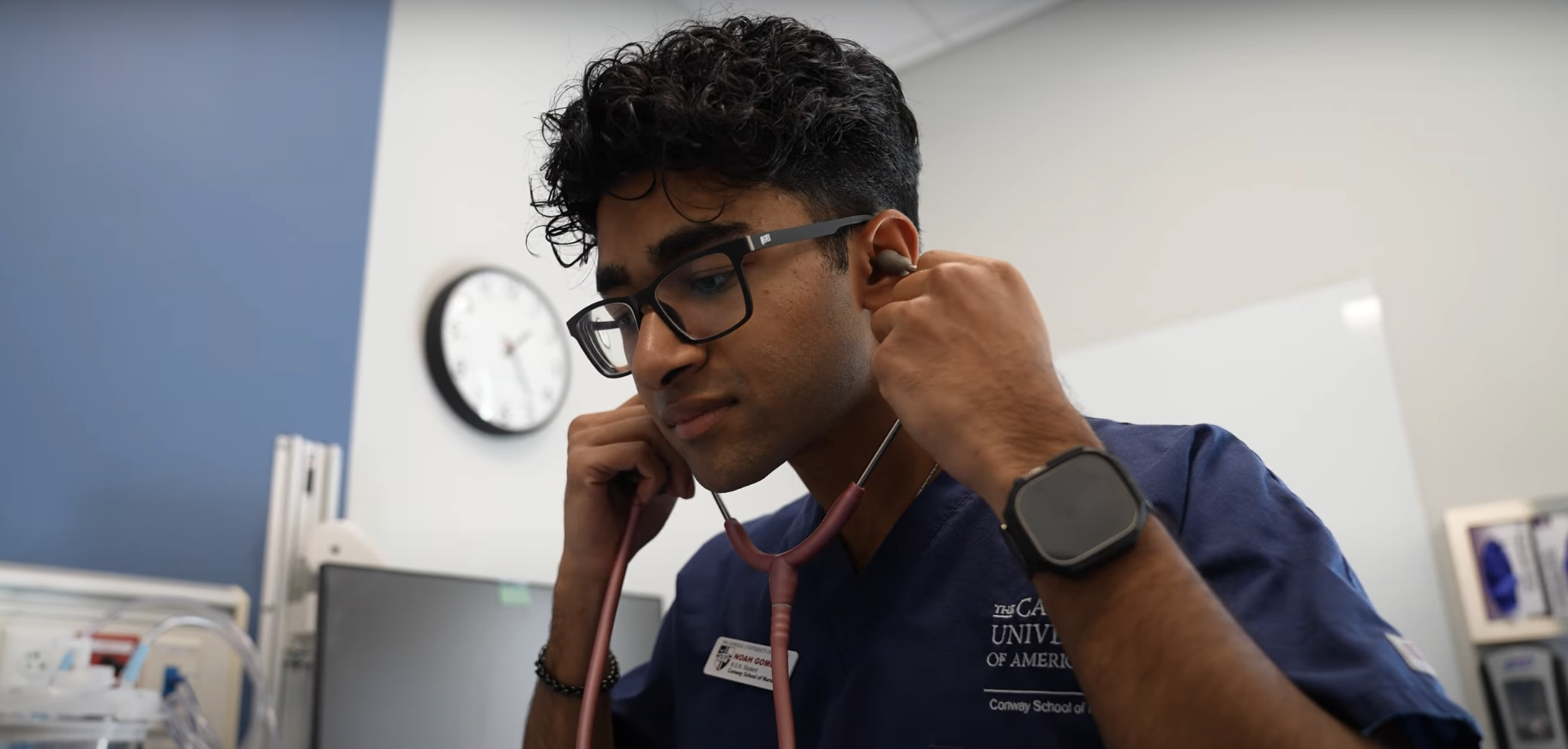 Noah Gomes video thumbnail, with him wearing blue Catholic University scrubs