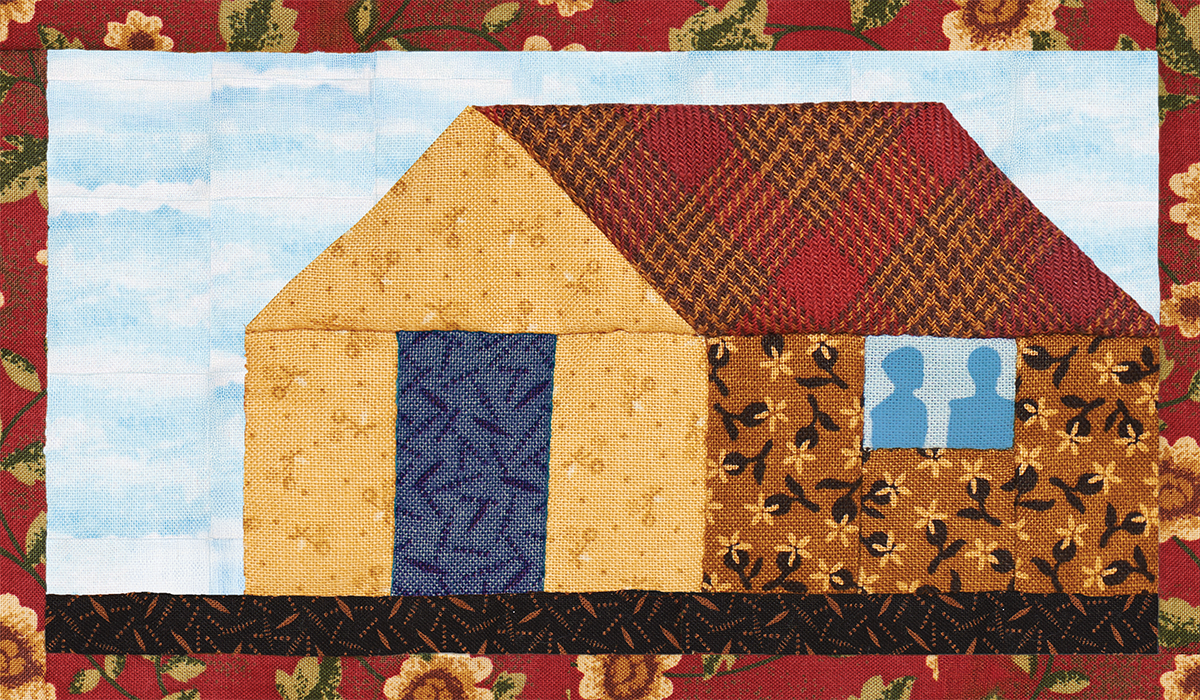 A quilt made from scrap fabric represents a house. Through the window, the shadow of two people in blue.