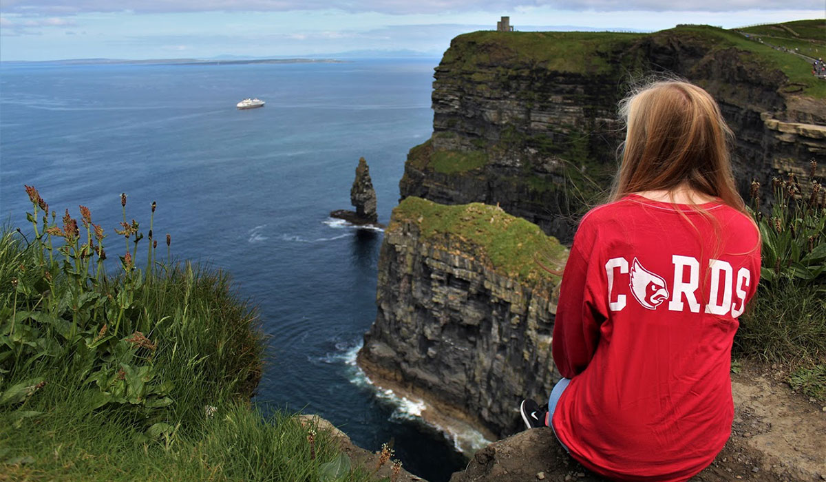 student sitting on a cliff over a body of blue water