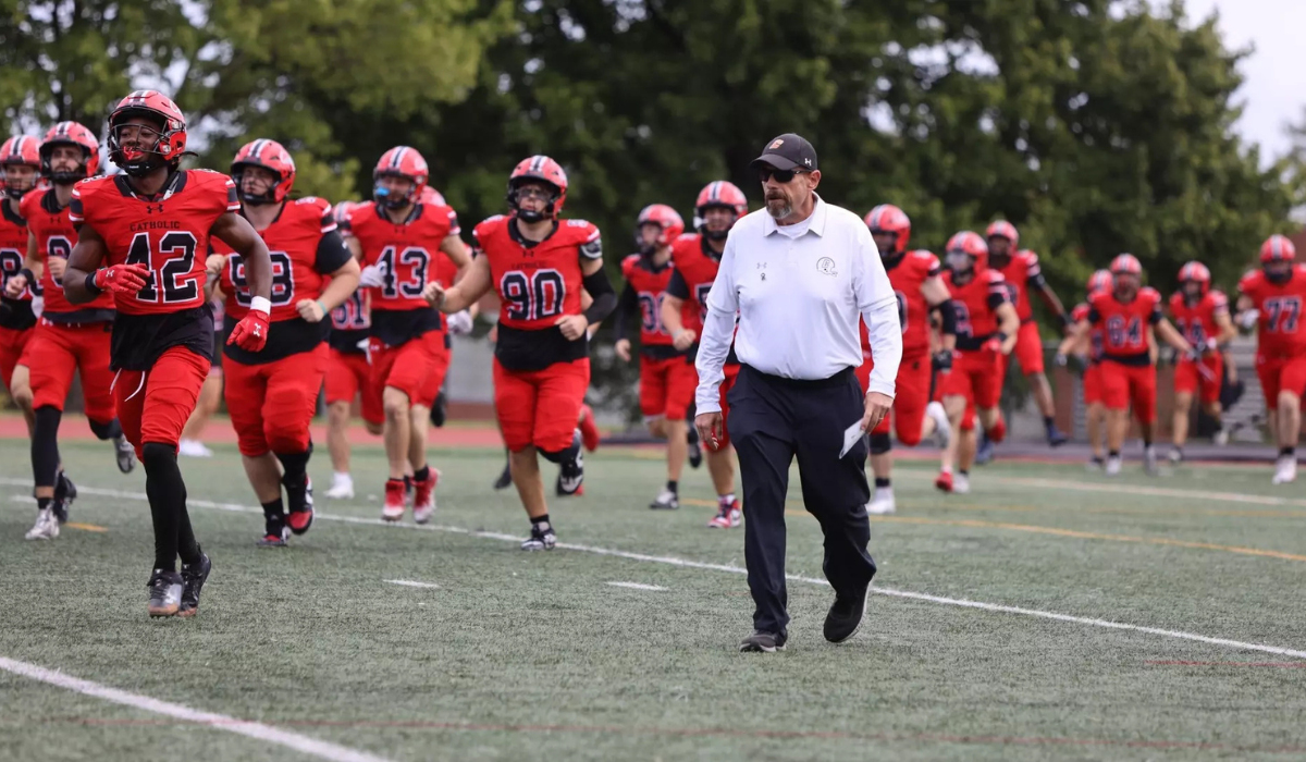 Coach Gutelius walking alongside the Cardinals football team on the field.