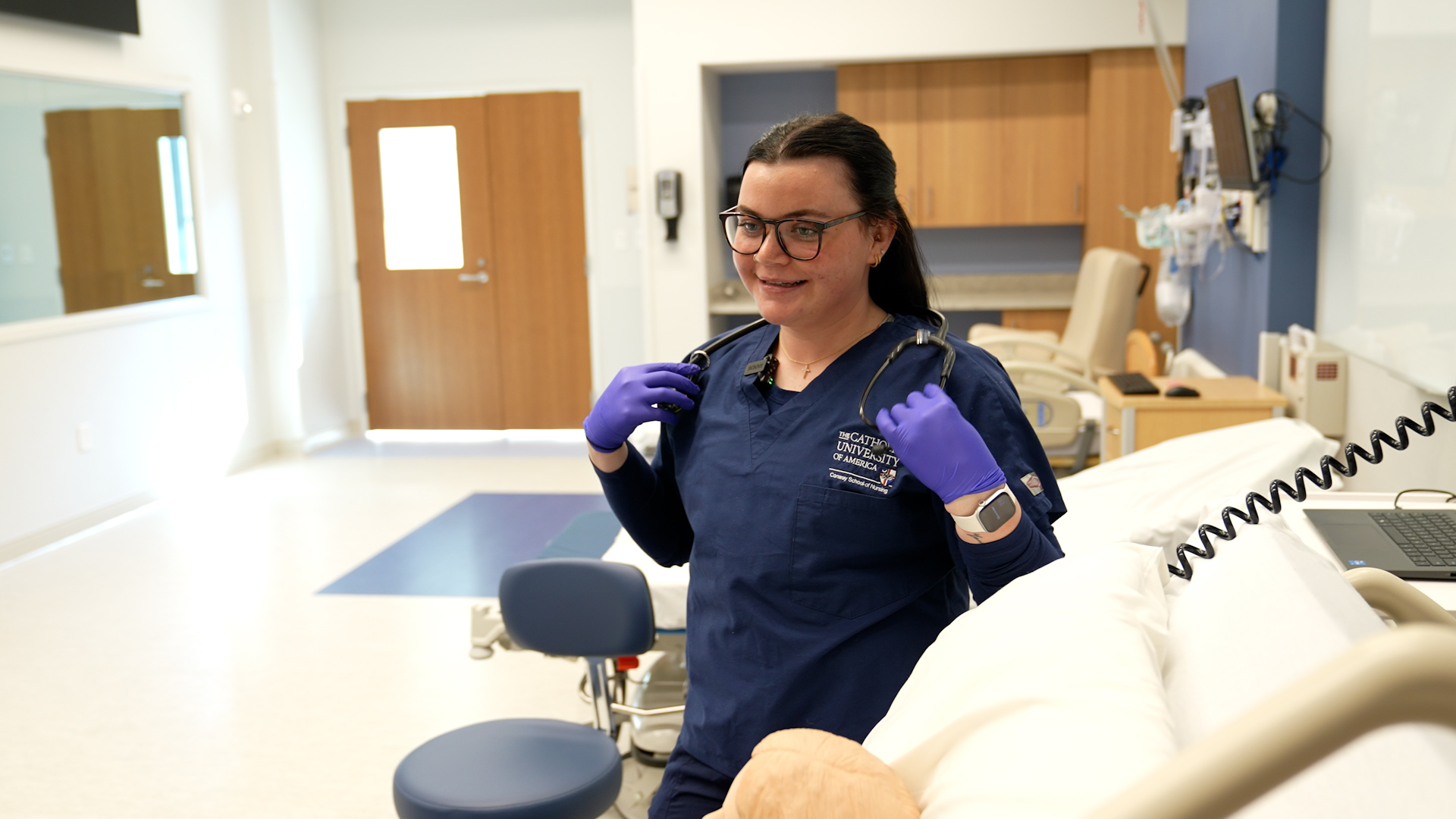 Megan Stake in her blue scrubs in front of a mannequin at the simulation lab.