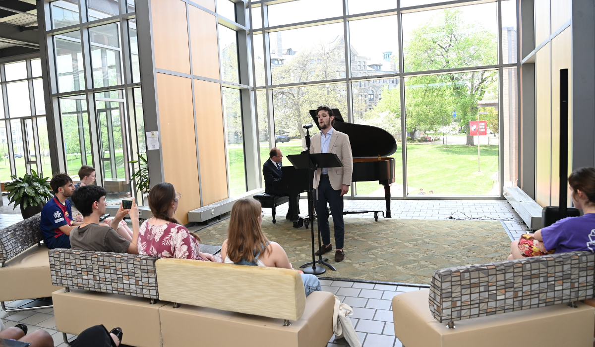 A vocal performance student is performing at URD2026. He is standing in front of a piano.