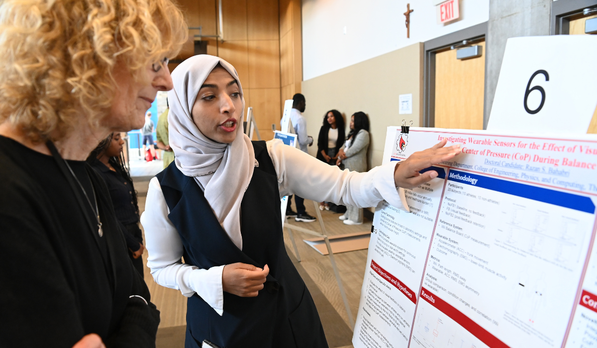 A student is showcasing her poster presentation at URD 2026.