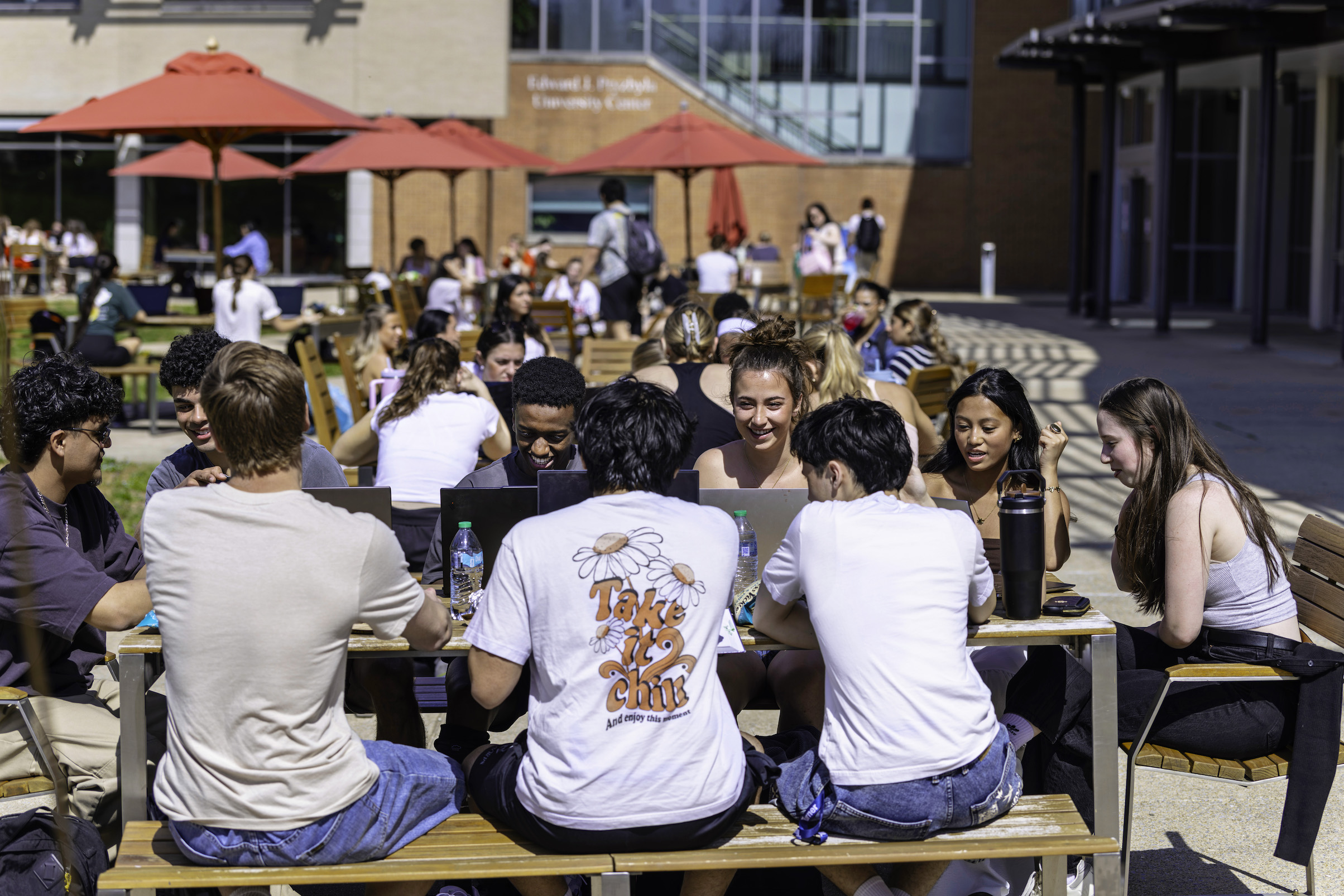 group of students outside at a picnic table, on laptops