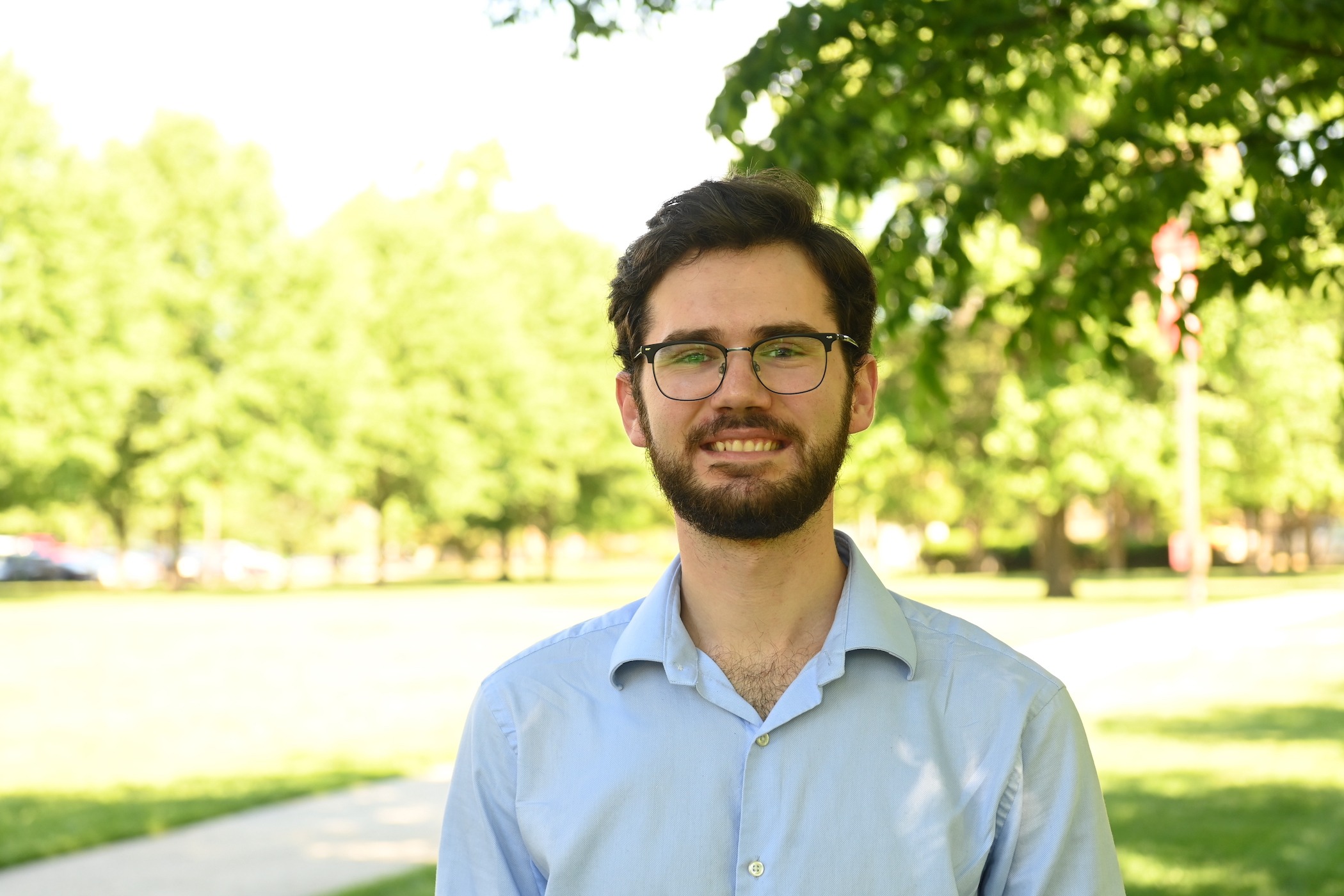 Student smiles on campus, wearing light blue and glasses