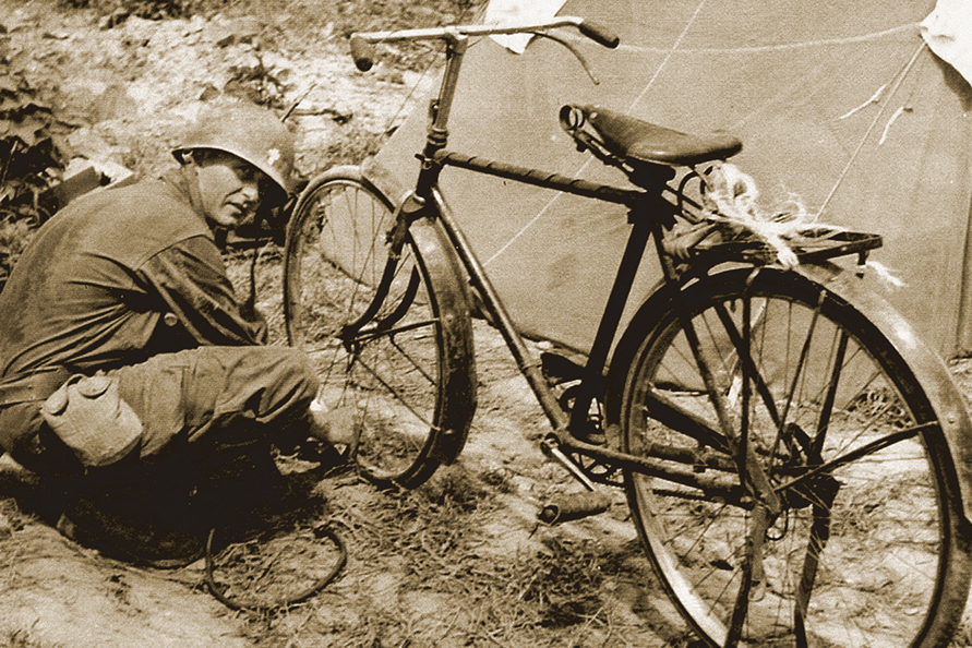 Fr. Emil Kapaun in his military uniform fixing a bicycle