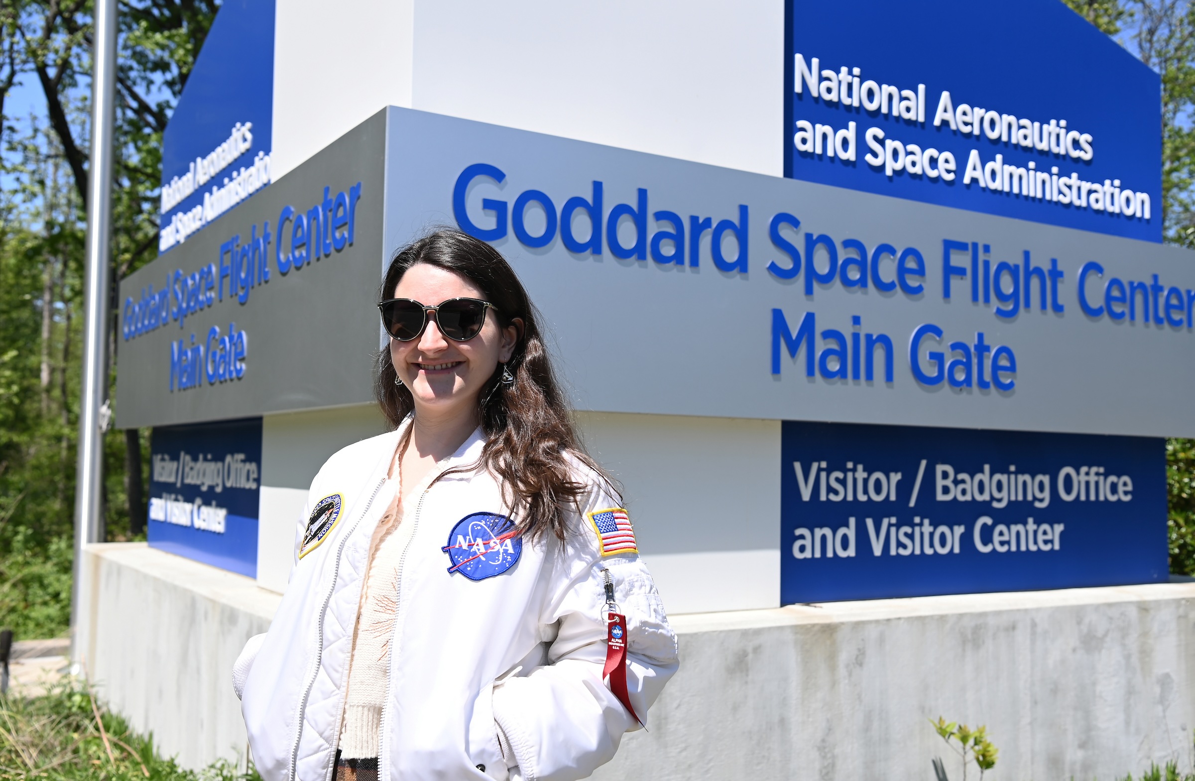 Carina Alden stands in front of an entrance sign for Goddard Space Flight Center