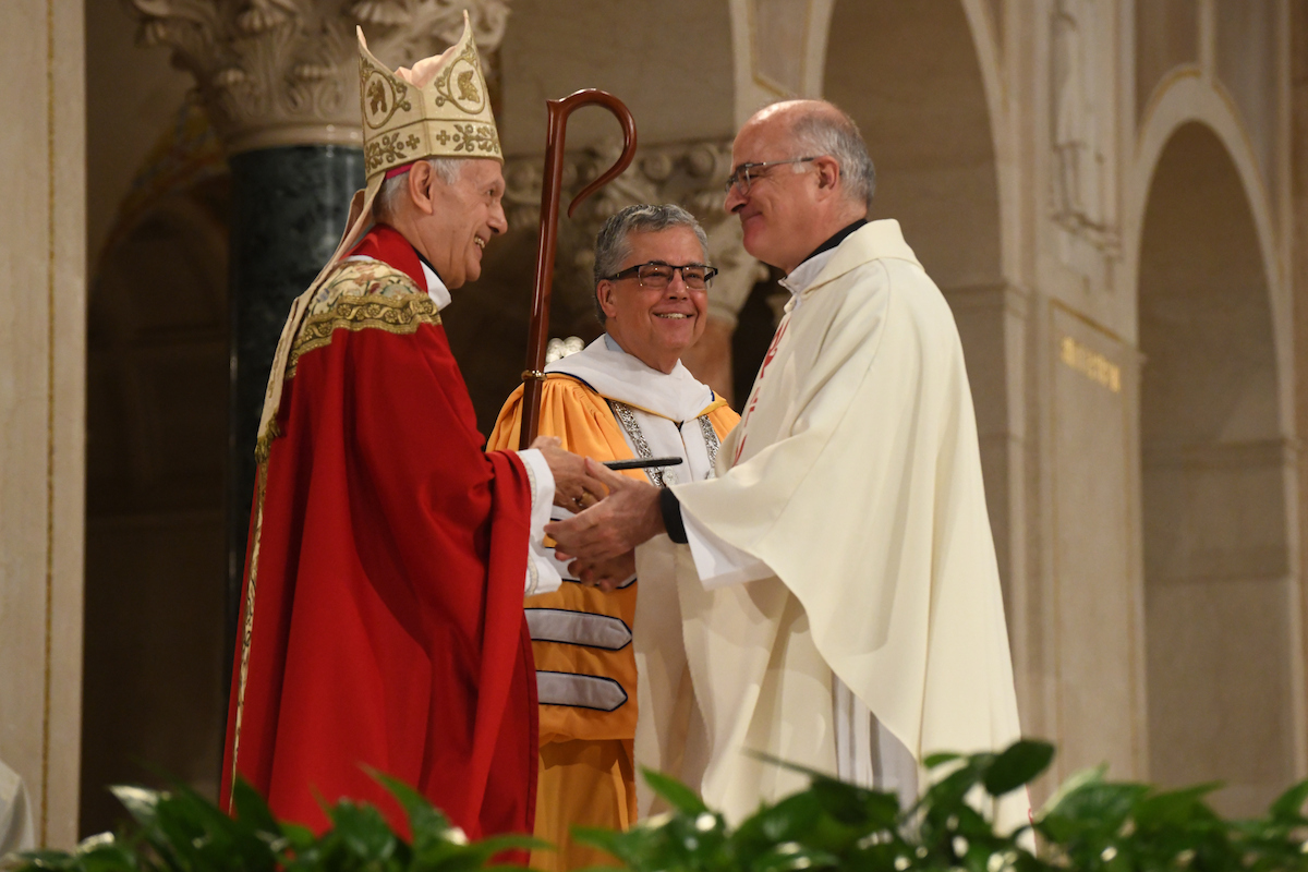 Archbishop Caccia shakes hands with Fr. Jose Norriega as President Peter Kilpatrick looks on