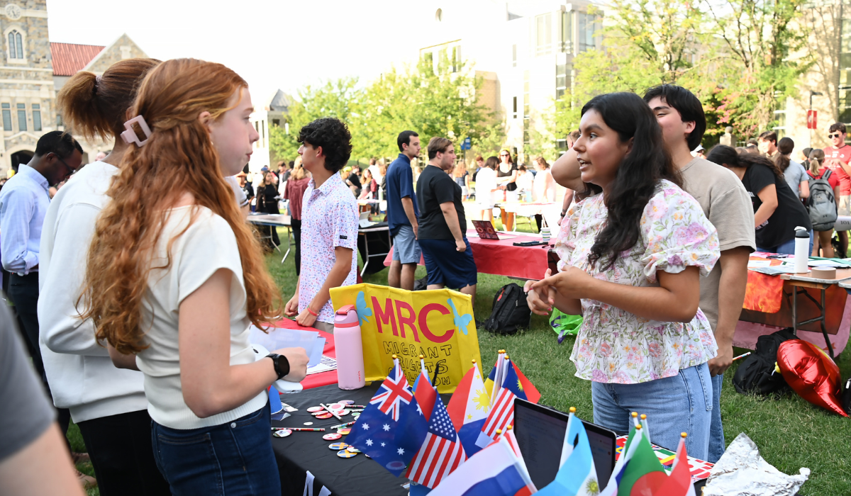 A student talks with a representative at the Migrant Rights Coalition (MRC) table, decorated with small flags from countries around the world, during Fall Fest on the University Lawn.