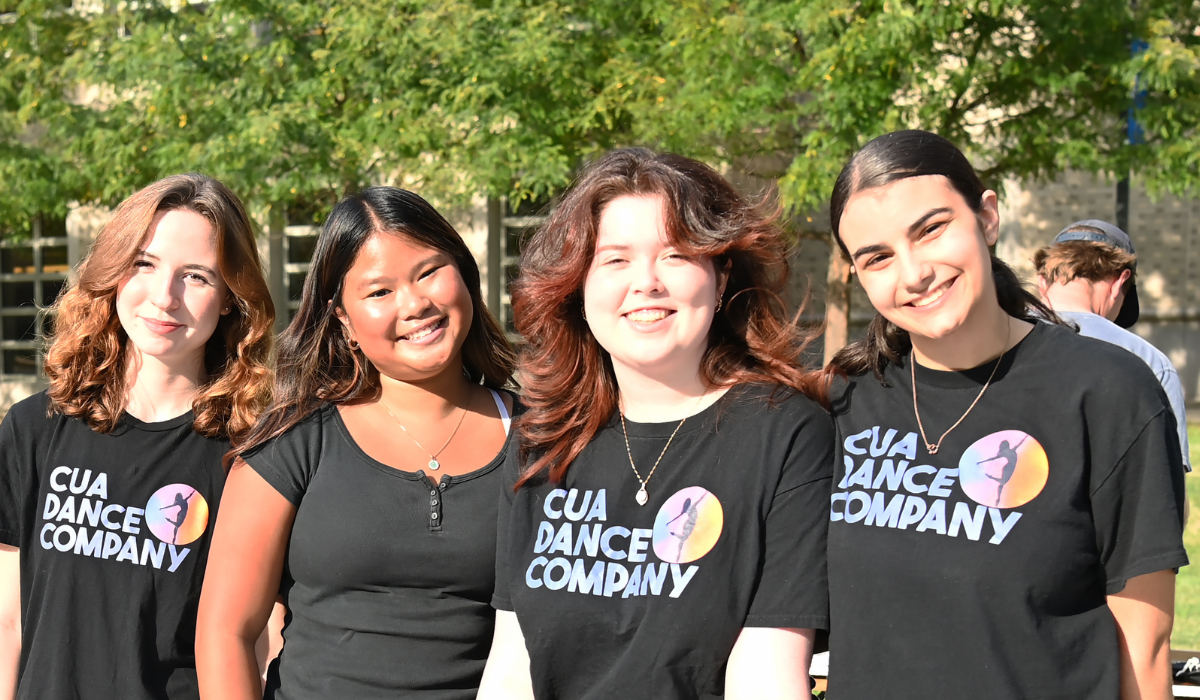 Four members of the CUA Dance Company pose together in matching black T-shirts at their table during Fall Fest on the University Lawn.