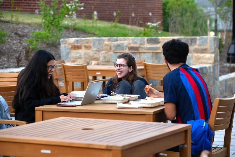 students smiling and talking at a picnic table outdoors on campus