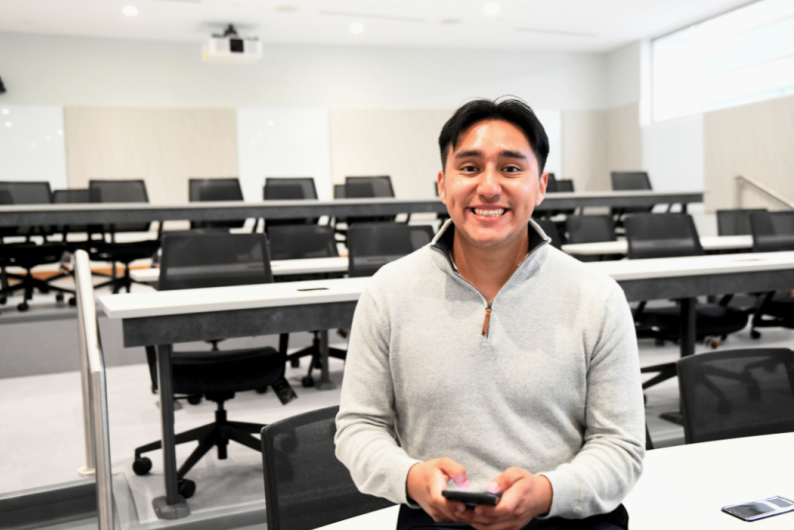 Luis Garcia Abundis is sitting in an empty Catholic University classroom. He is wearing a grey sweatshirt.
