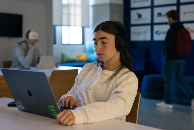 student with headphones on working on her laptop