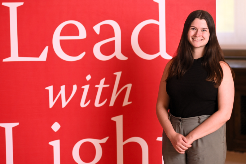 Maria Duffy is standing in front of a red Catholic University background.