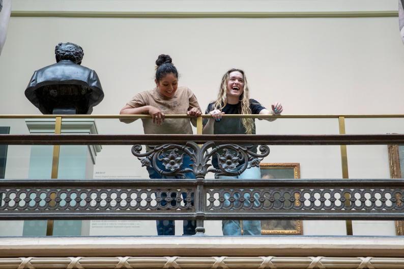 students standing on a balcony in a museum and laughing