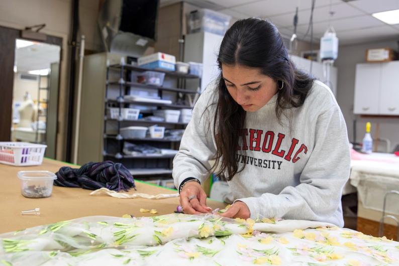 girl sewing a piece of fabric in a room on campus