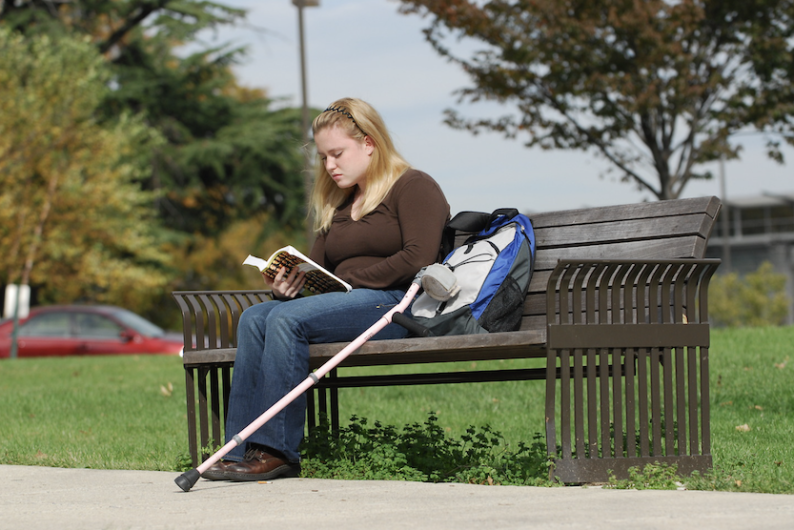 girl sitting on bench with a crutch