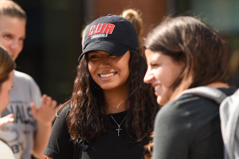 smiling student in a black CUA Cardinals hat