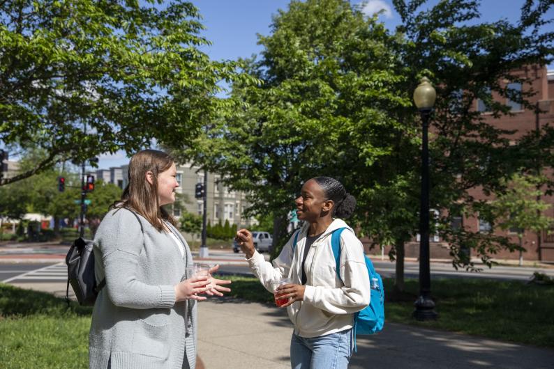 two students conversing on a sidewalk in fall