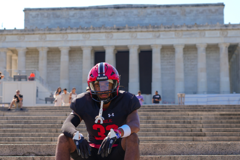 Malachi is sitting at the Lincoln Memorial wearing his football gear.