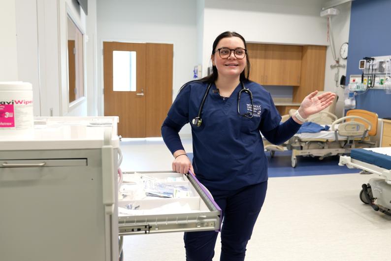Megan Stake is wearing her blue Catholic University scrubs in a simulation lab.