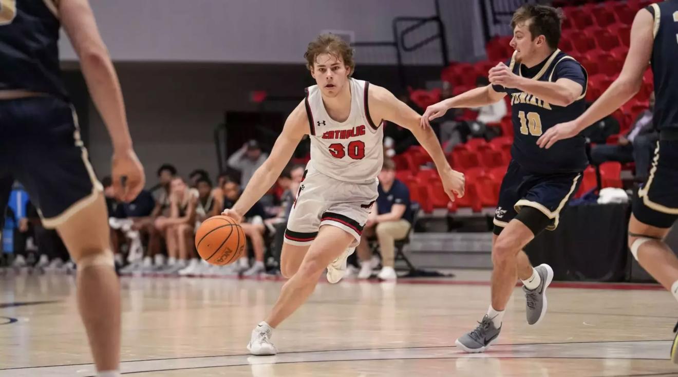 Catholic University men's basketball player dribbling down the court.