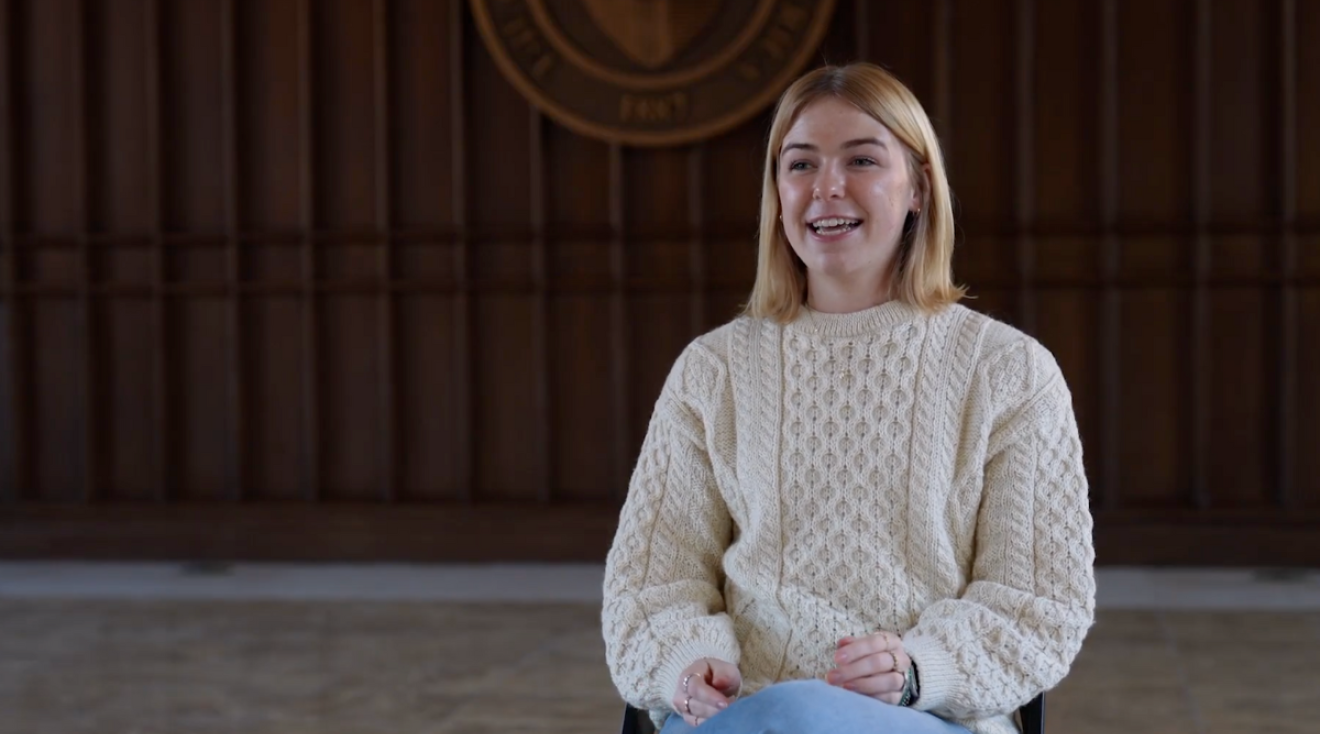 Catherine is sitting in Heritage Hall, wearing an Aran cable-knit sweater.
